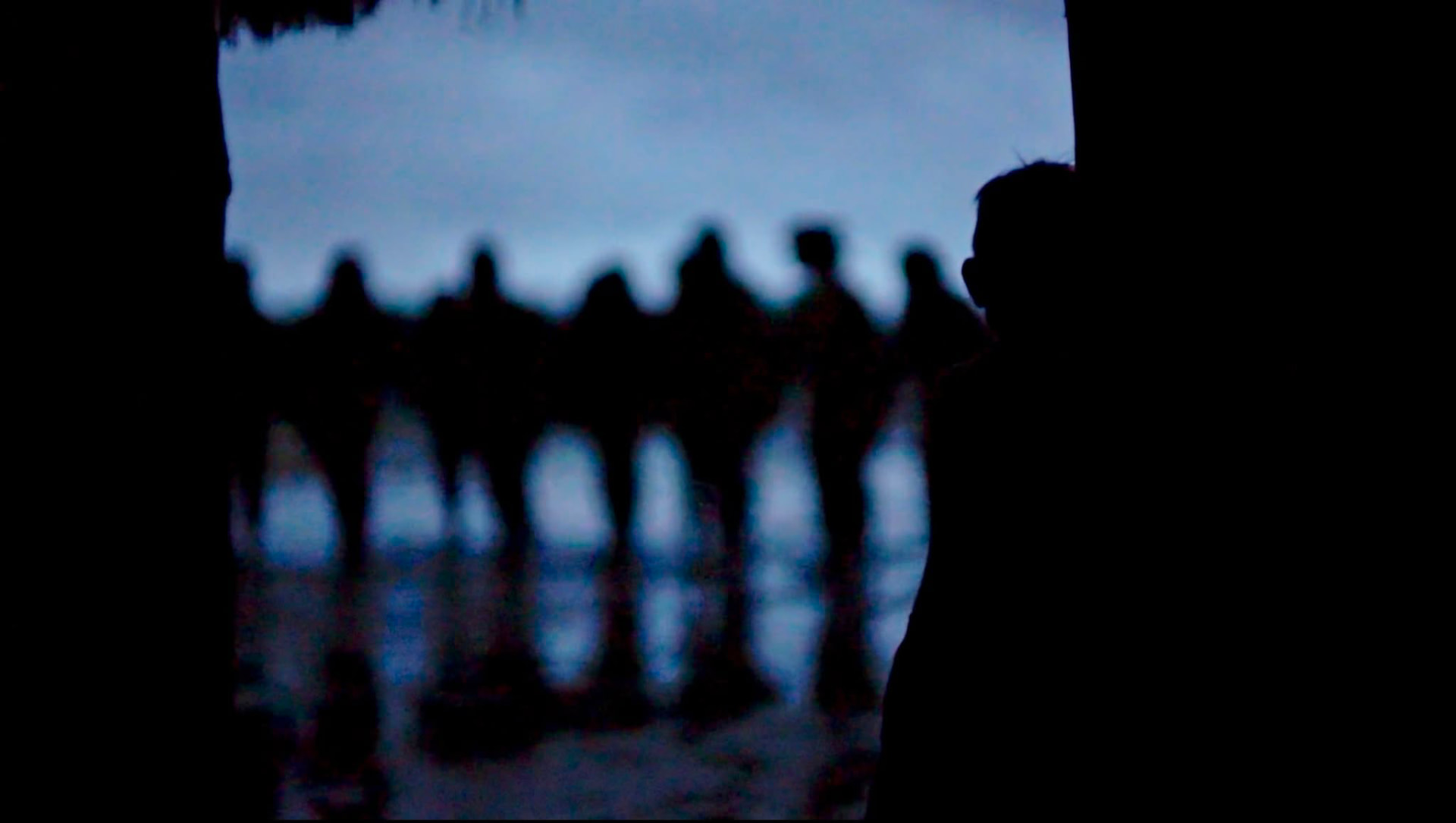 Silhouettes seen from a dark doorway across wet ground at dusk