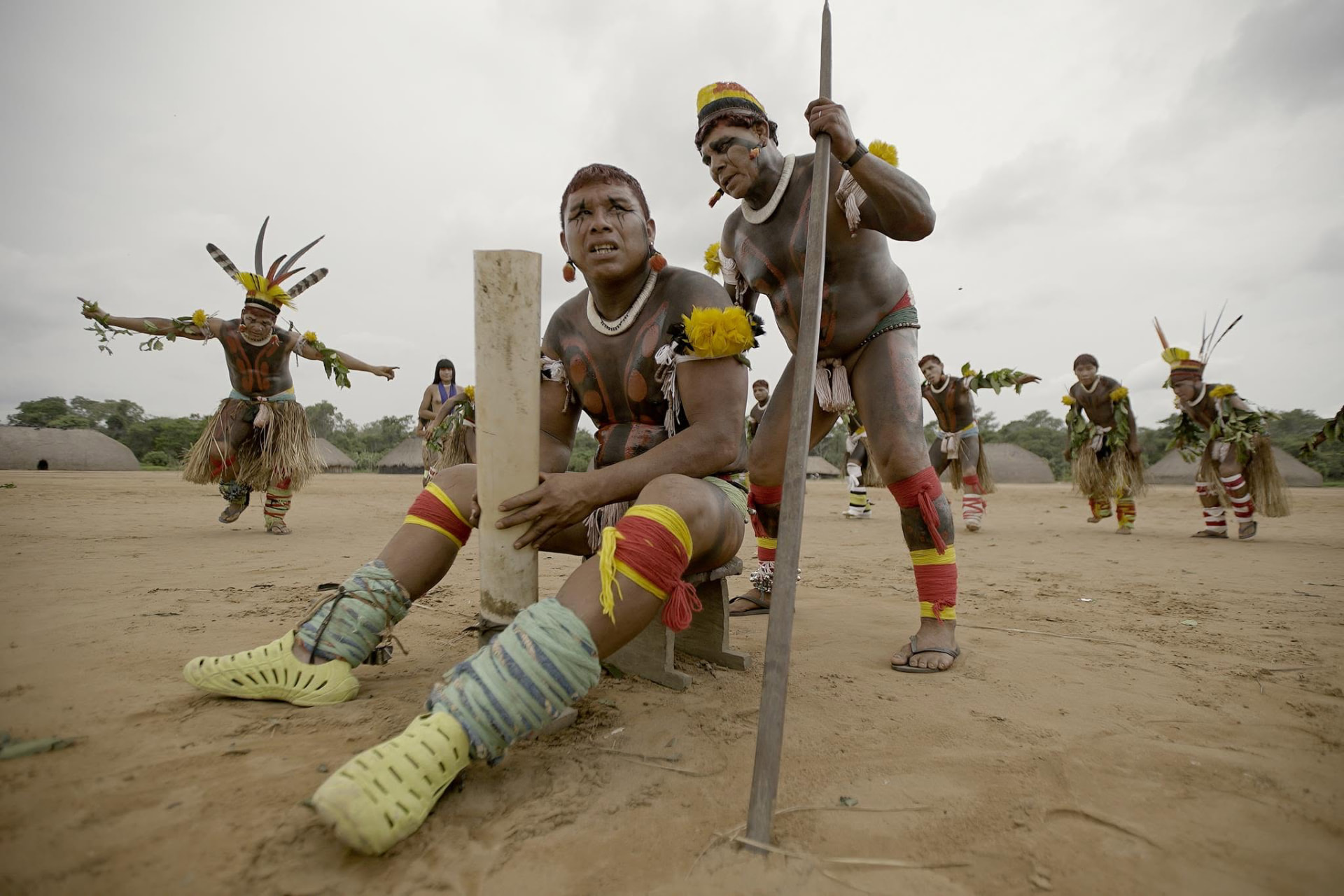 Xingu men in body paint and feathered headdresses in a village plaza