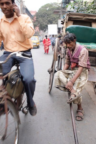 A man resting on the shafts of a hand-pulled rickshaw on a city street