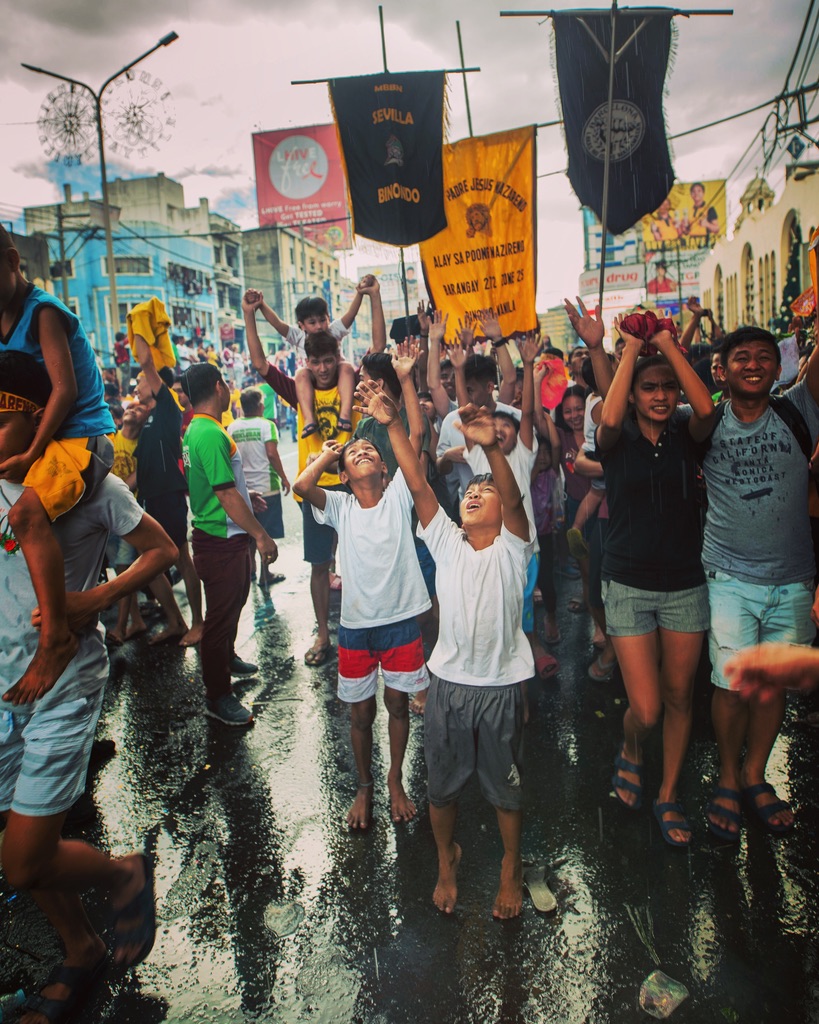 Children reaching up in a rain-soaked street procession