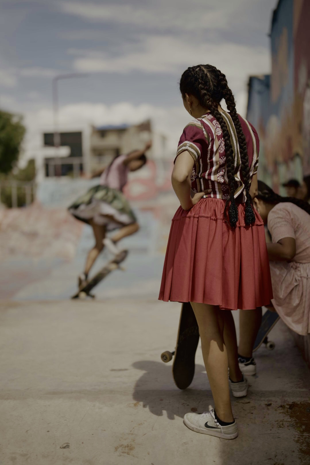 A young skater in traditional dress watching a trick at a skate park
