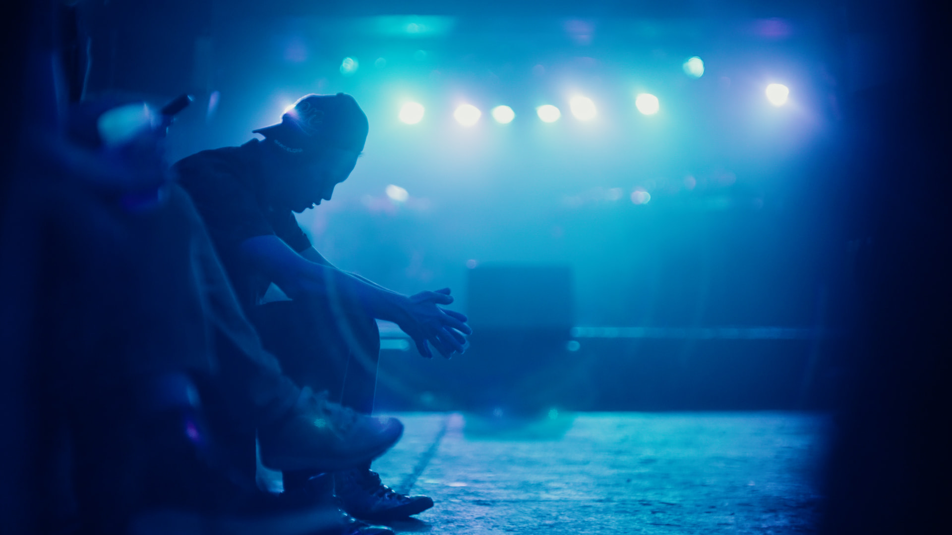 Lucas seated backstage in blue stage light, head bowed