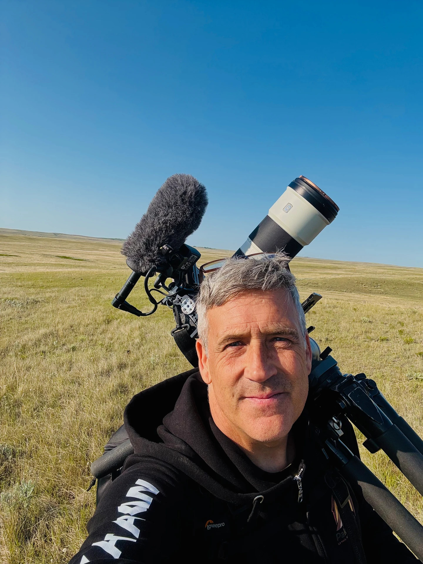 Éli Laliberté on location in open grassland, camera gear over his shoulder